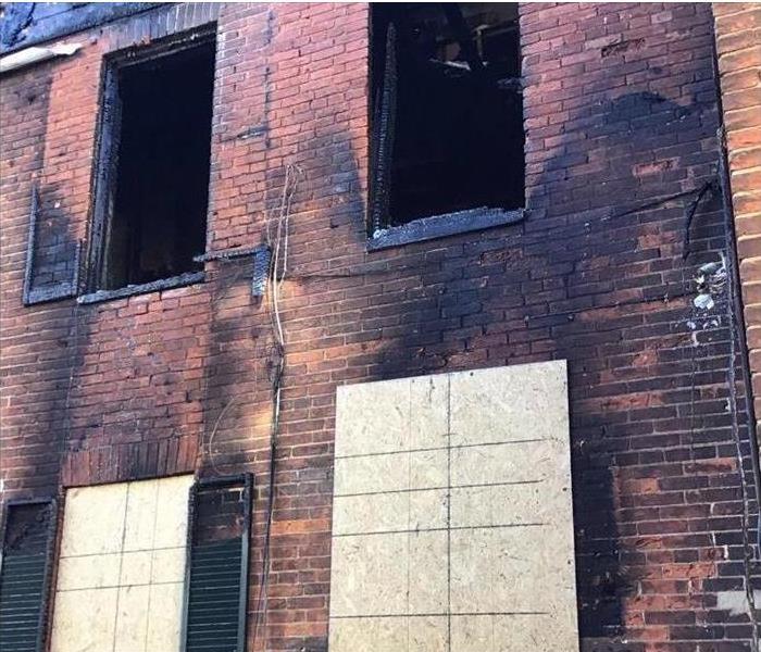 side of a brick building with fire damage. The window is boarded up